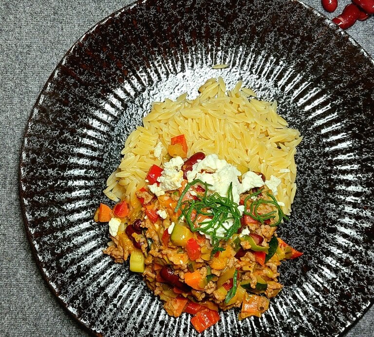 Reisnudeln auf schwarzem Teller und grauem Untergrund, mit mediterranem Gemüse an der Seite. | © EAT CLUB/ Felix Scheel