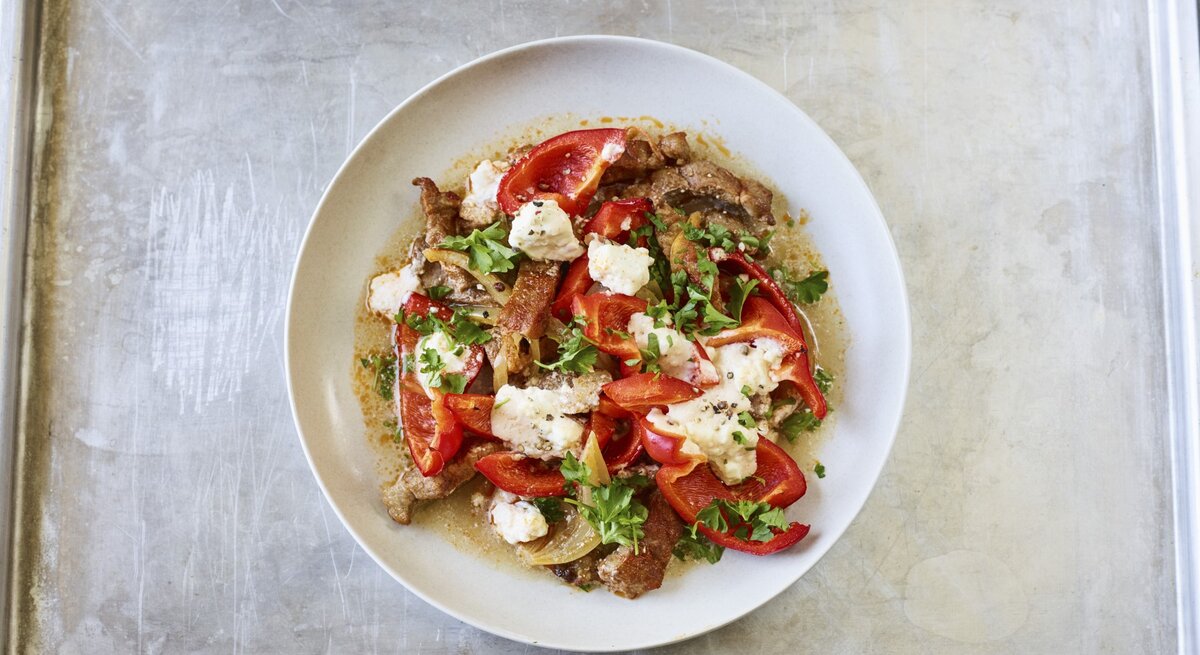 Ofen-Gyros mit Paprika und Feta vom Blech in einem tiefen Teller. Dieser steht auf einem Blech. 