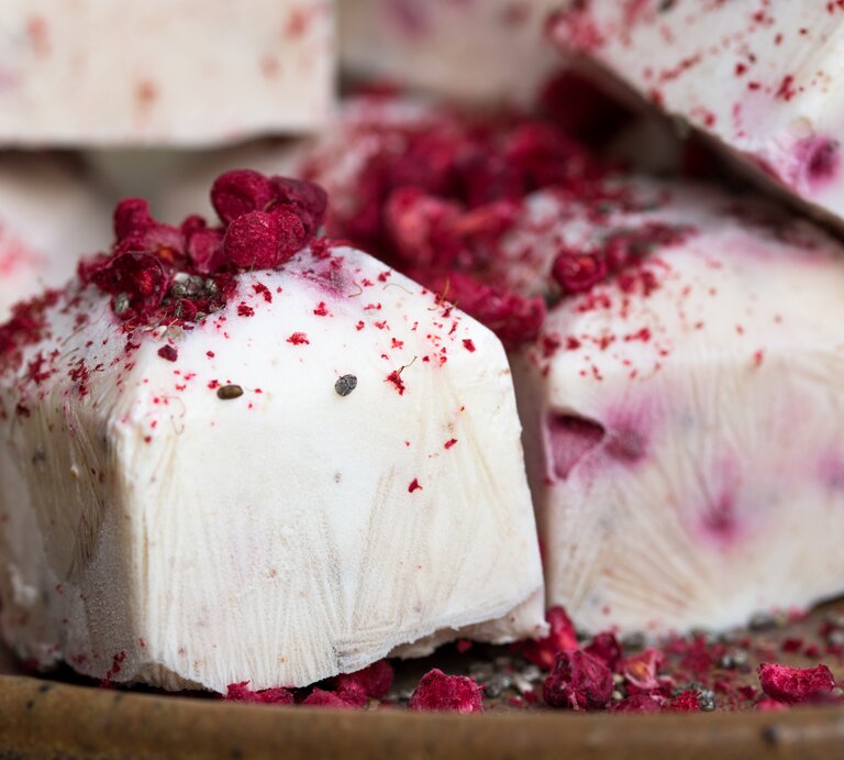 Mehrere Frozen Himbeer-Joghurt-Würfel liegen auf einem Untergrund auf Holz. Es handelt sich um gefrorene Sahne-Joghurt-Würfel mit Himbeeren. | © Shutterstock / Gudafuda
