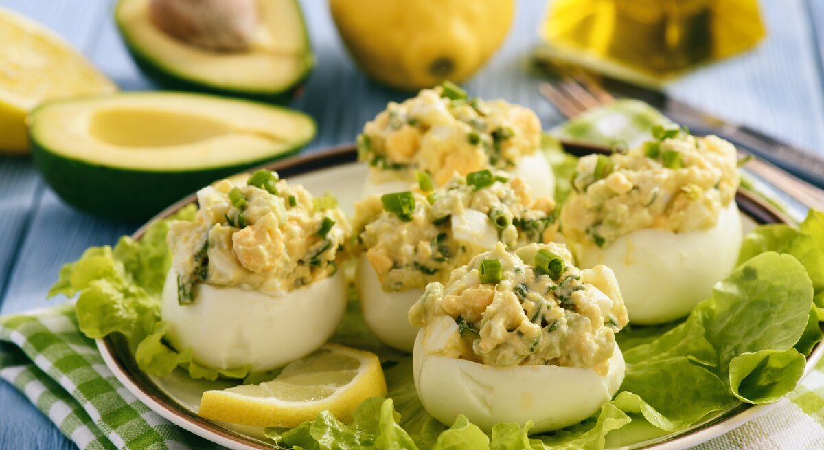 Gefüllte Eier mit Avocado auf Salatblättern umrundet von den Zutaten.