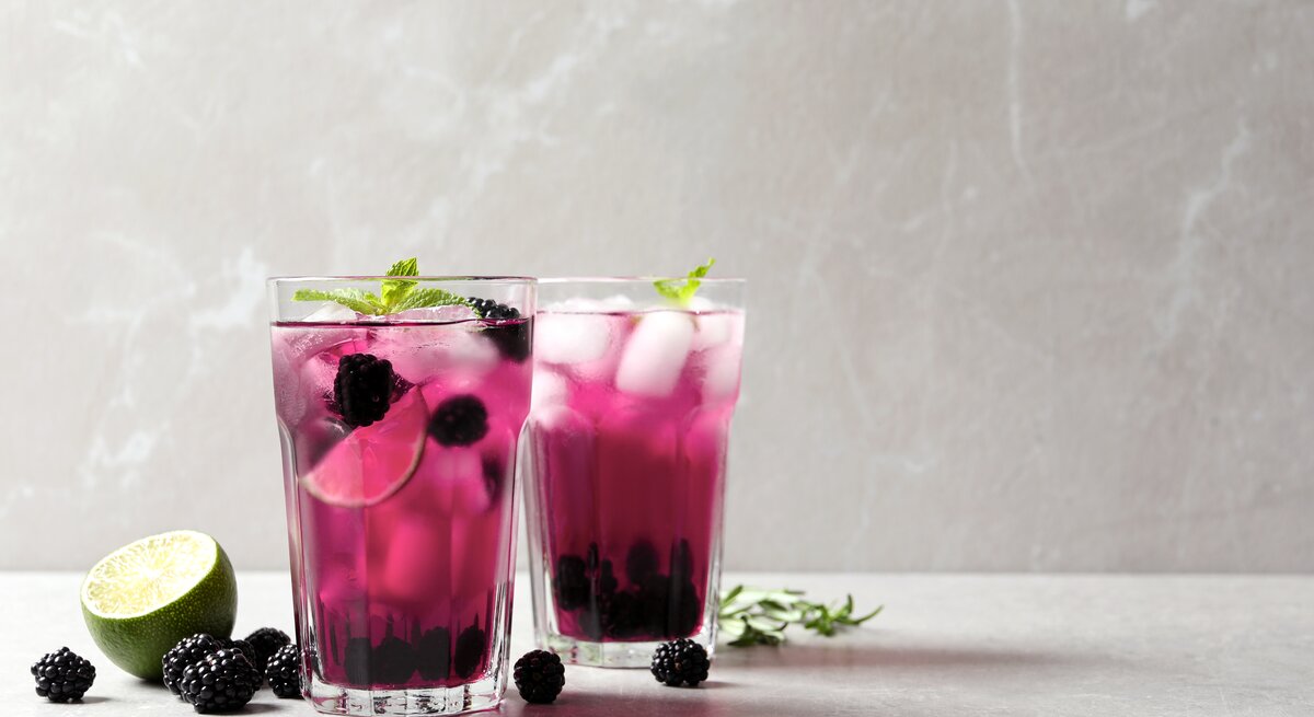Zwei Gläser Brombeer-Fizz mit frischen Beeren und Limettenscheiben, außerdem Minze.