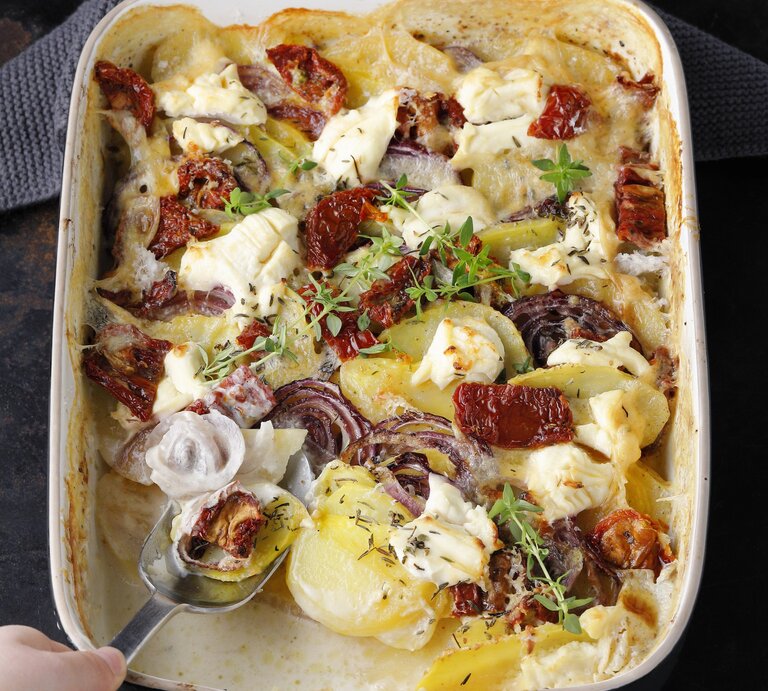 Kartoffelgratin mit getrockneten Tomaten, roter Zwiebel und Thymian, mit Käse überbacken in einer großen Auflaufform auf einem dunklen Tisch.  | © StockFood / Gräfe & Unzer Verlag / mona binner PHOTOGRAPHIE