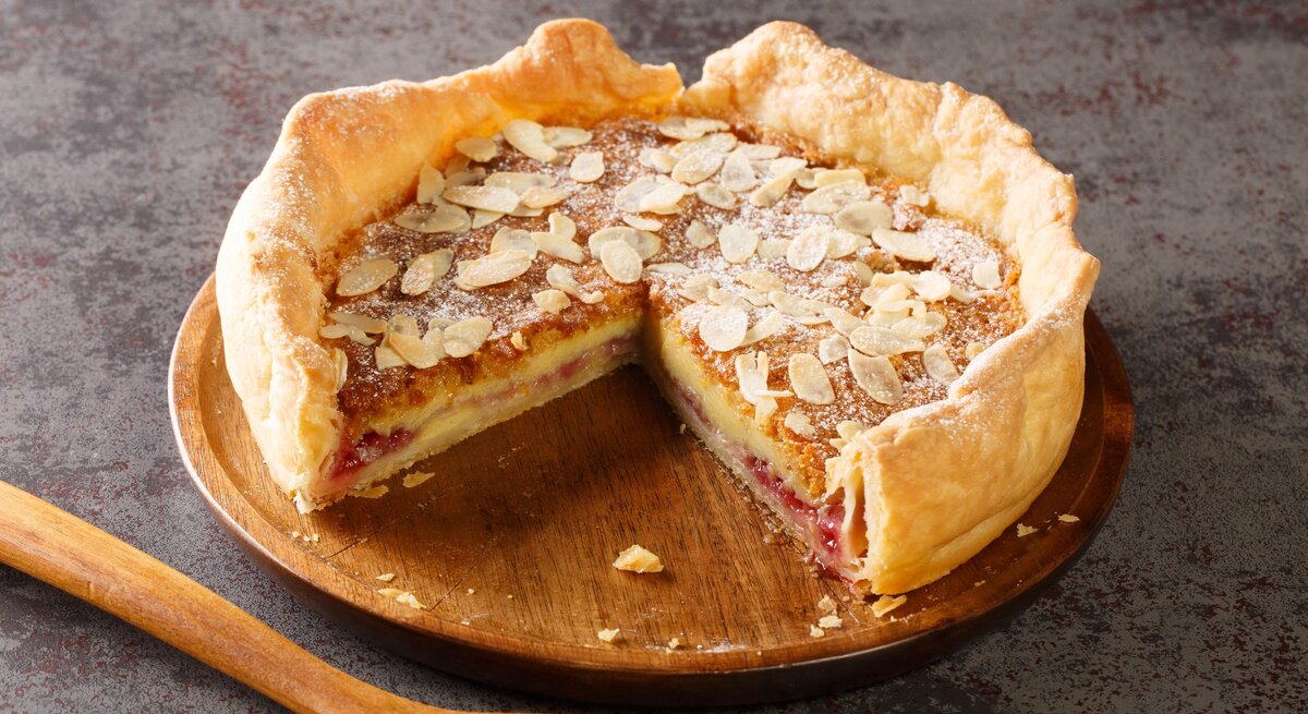 Ein Bakewell-Pudding auf einem Holzbrett auf einem grauem Steintisch.