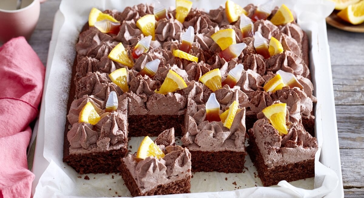 Auf einem Blech ist ein  Limo-Kuchen gebacken. Er ist mit Cola Fruchtgummis und Orangenstücken belegt. 