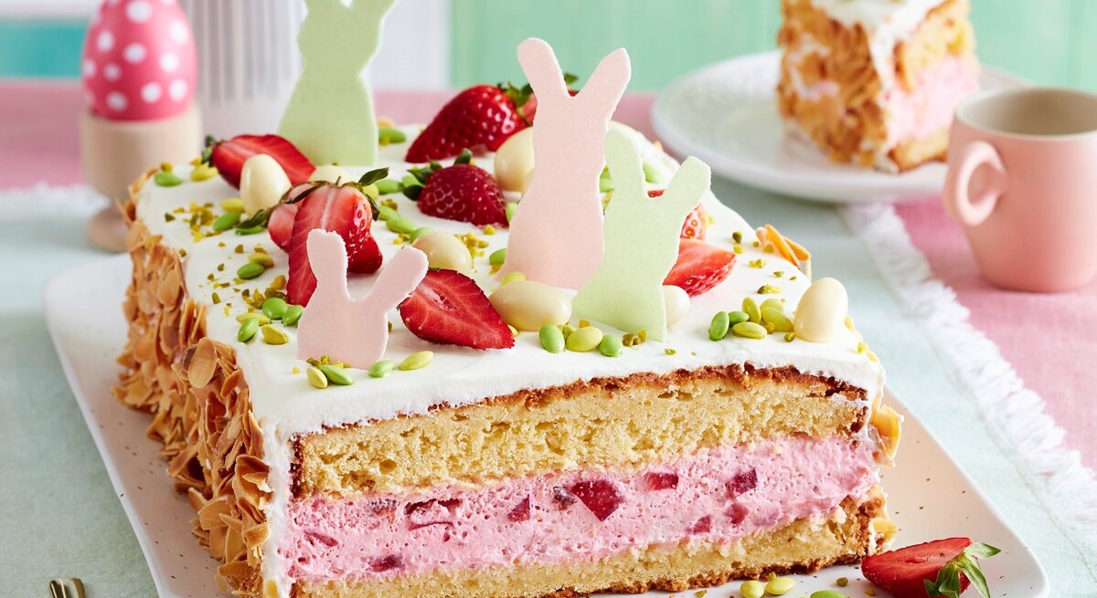 Auf einer Kuchenplatte ist eine Erdbeer-Ostertorte serviert. Sie ist mit Erdbeeren und Osterhasen aus Esspapier dekoriert.