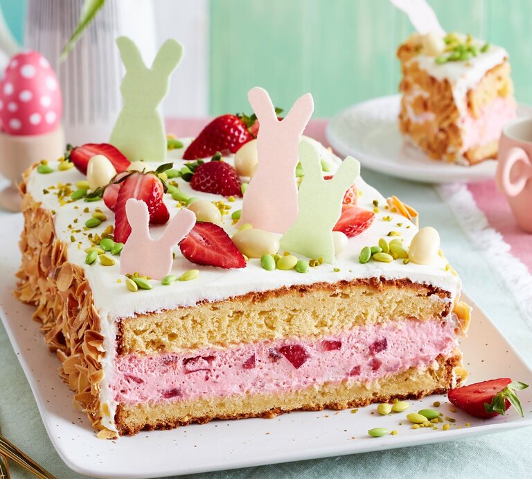 Auf einer Kuchenplatte ist eine Erdbeer-Ostertorte serviert. Sie ist mit Erdbeeren und Osterhasen aus Esspapier dekoriert. | © EAT CLUB / Isabell Triemer