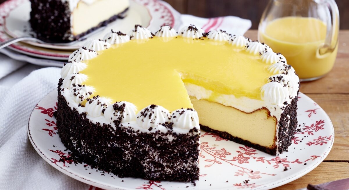 Ein angeschnittener Kakaokeks-Käsekuchen, daneben ein Teller mit einem Stück davon sowie ein Milchkännchen.