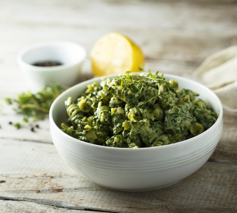 Eine weiße Schale Spirelli mit Rosenkohl und Tofu, garniert mit frischem Oregano. Im Hintergrund unscharf eine halbe Zitrone und eine kleine Schale sowie einige Kräuter. | © Getty Images/ Mariha-kitchen