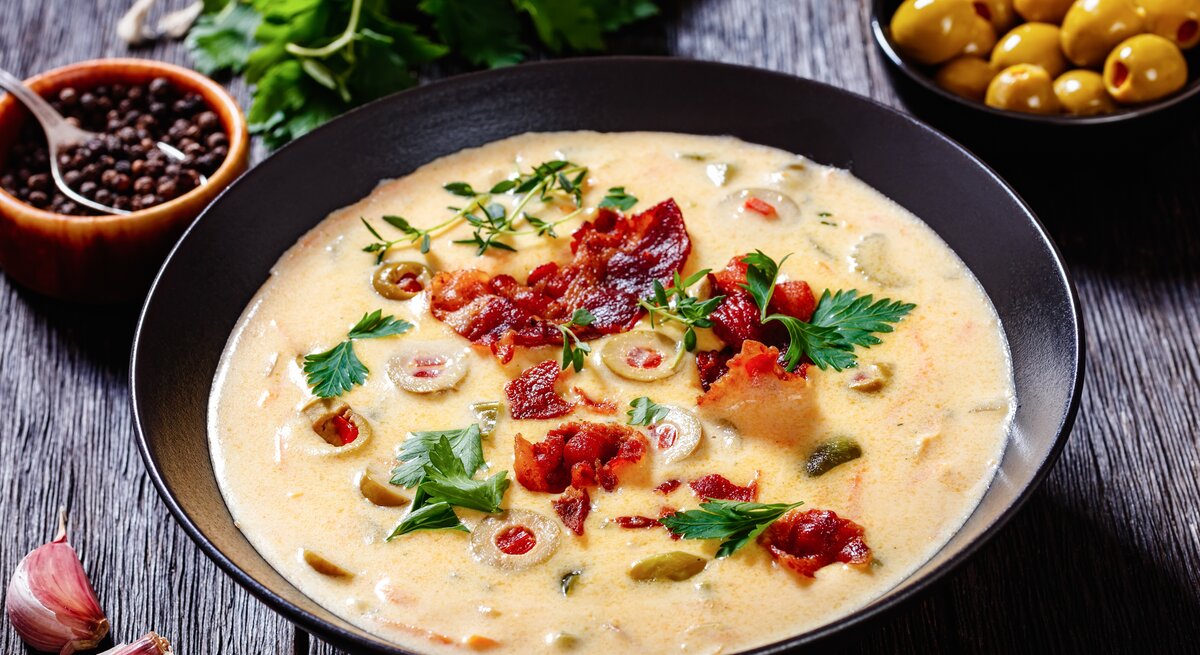 Käse-Bier-Suppe mit Bacon in schwarzer Schale auf schwarzem Holz. 
