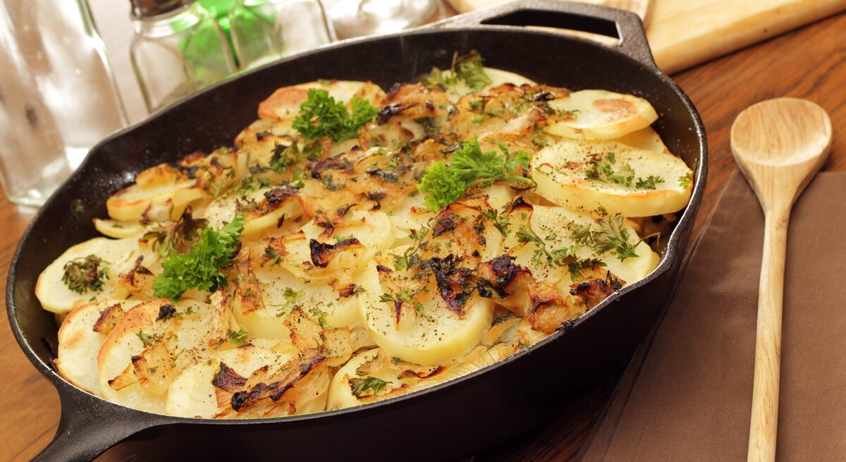 Kartoffeln Lyonnaise in gusseiserner Pfanne auf Holz. 