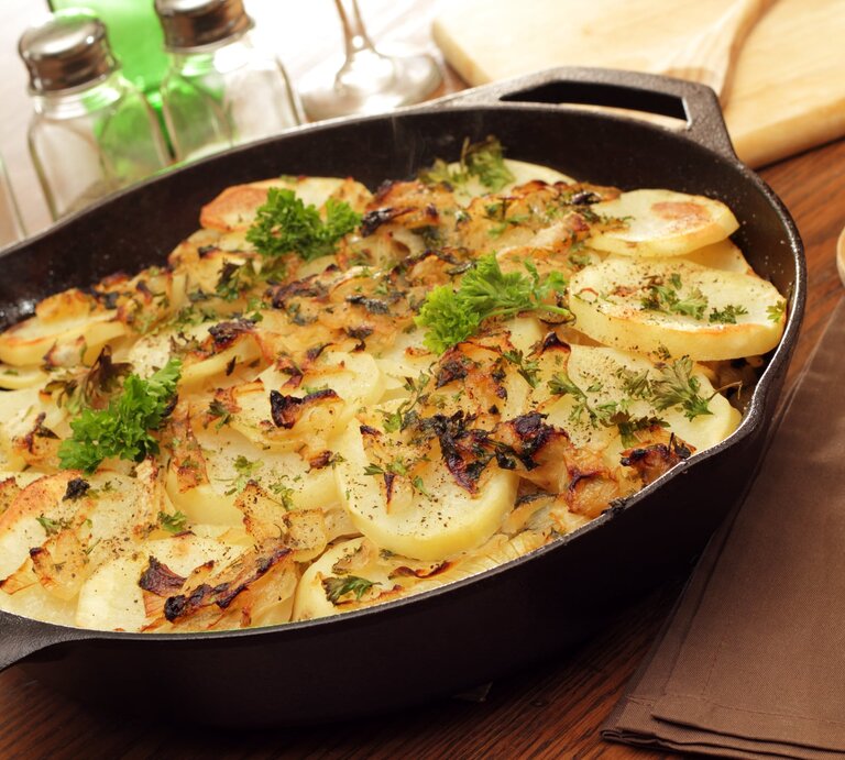 Kartoffeln Lyonnaise in gusseiserner Pfanne auf Holz.  | © Getty Images/wsmahar