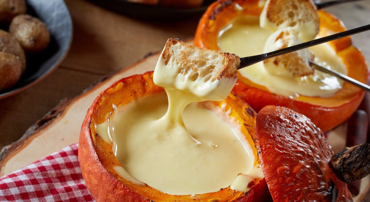 Käse-Fondue im Kürbis auf einem rustikalen Tisch mit rot-weiß-karierter Tischdecke.