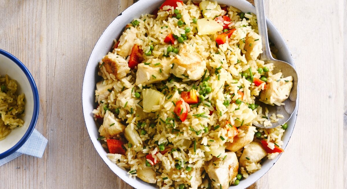 In einer Schüssel ist ein Reissalat mit Huhn, Ananas und Tomaten angerichtet. Er ist mit Schnittlauch überstreut.