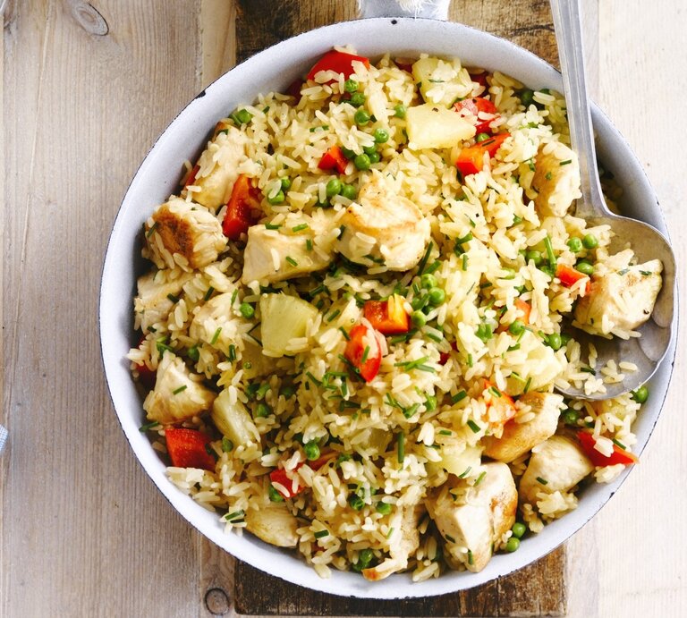 In einer Schüssel ist ein Reissalat mit Huhn, Ananas und Tomaten angerichtet. Er ist mit Schnittlauch überstreut. | © StockFood / PhotoCuisine