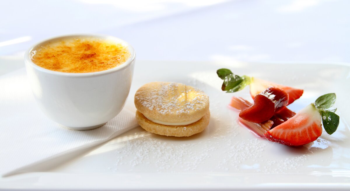 Ein weißer Tisch mit der Crème brûlée und etwas Dekoration. Alles von der Seite fotografiert.