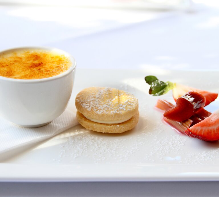 Ein weißer Tisch mit der Crème brûlée und etwas Dekoration. Alles von der Seite fotografiert. | © GettyImages/inesi