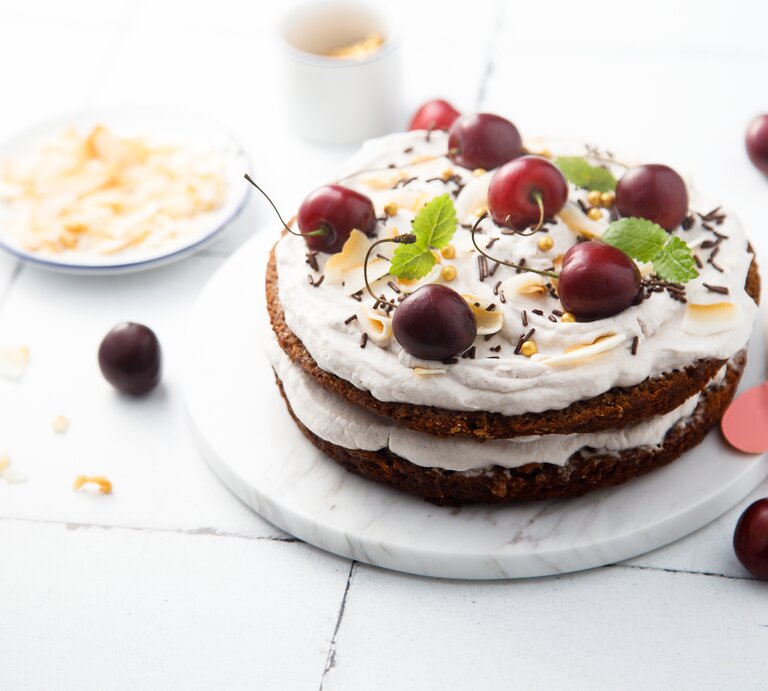 Schüttelkuchen nach Schwarzwälder-Kirsch-Art auf weißem, hölzernem Untergrund – umgeben von einigen Zutaten.  | © Shutterstock/MariaKovaleva