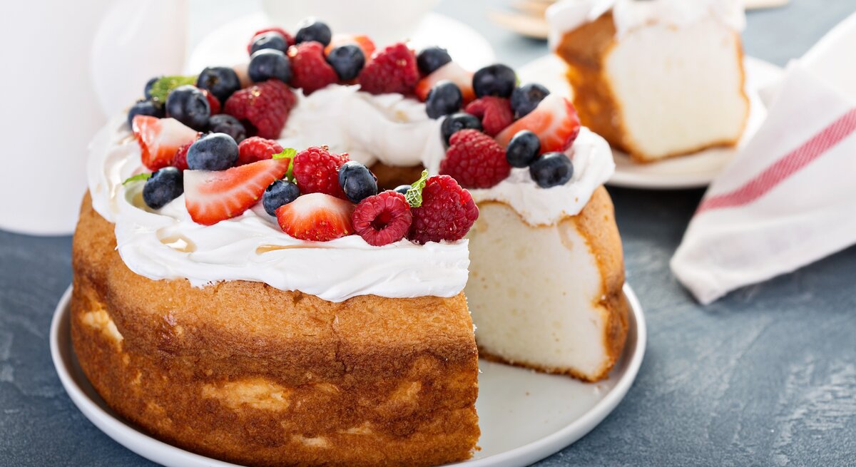 Heller Biskuitkuchen mit Creme und Beeren, angeschnitten, auf dunklem Untergrund. 
