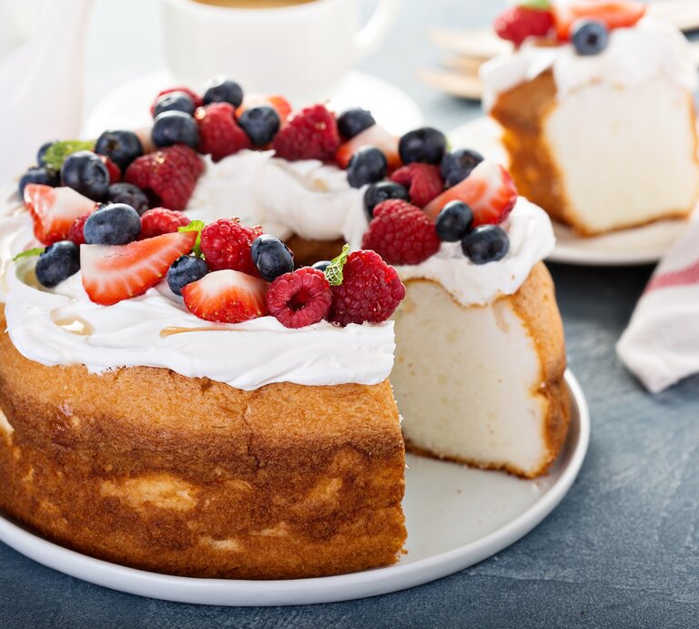 Heller Biskuitkuchen mit Creme und Beeren, angeschnitten, auf dunklem Untergrund.  | © imago/fahrwasser