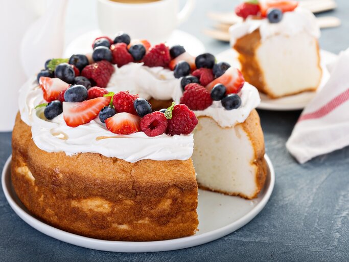 Heller Biskuitkuchen mit Creme und Beeren, angeschnitten, auf dunklem Untergrund.  | © imago/fahrwasser
