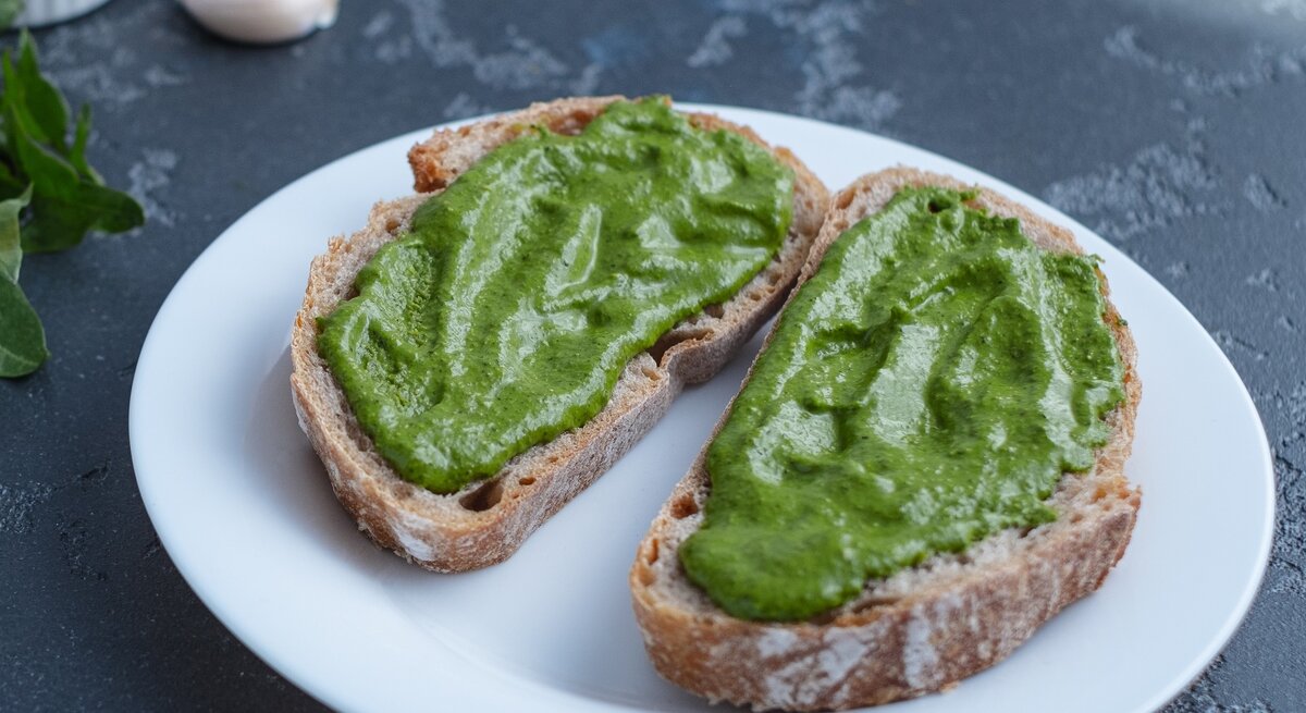 Ein weißer Teller mit zwei Brotscheiben und der grünen Avocado-Bärlauch-Creme.