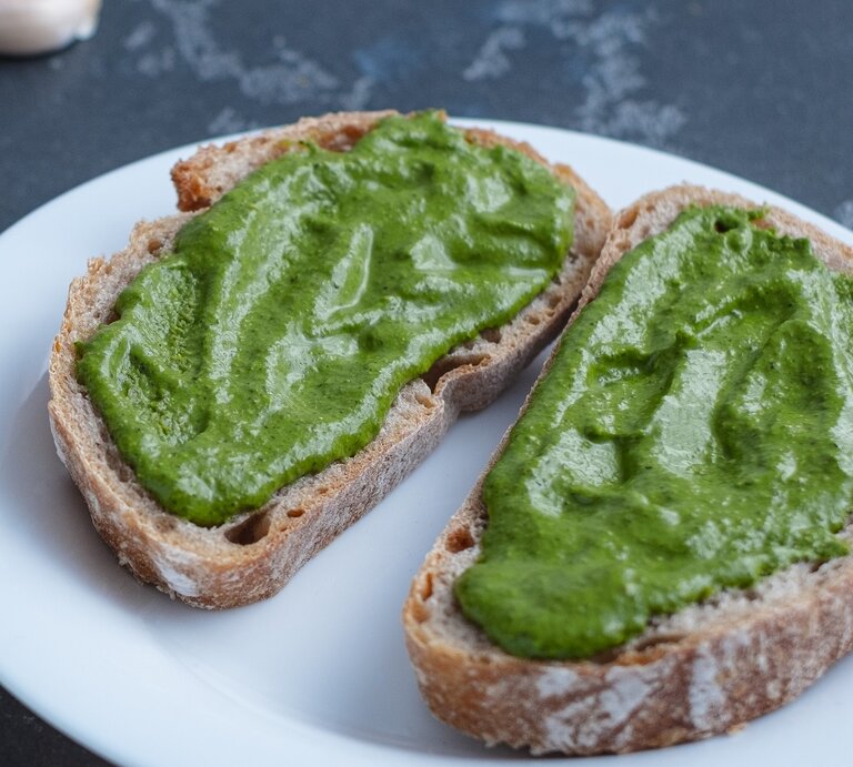 Ein weißer Teller mit zwei Brotscheiben und der grünen Avocado-Bärlauch-Creme. | © Shutterstock/ HalynaRom