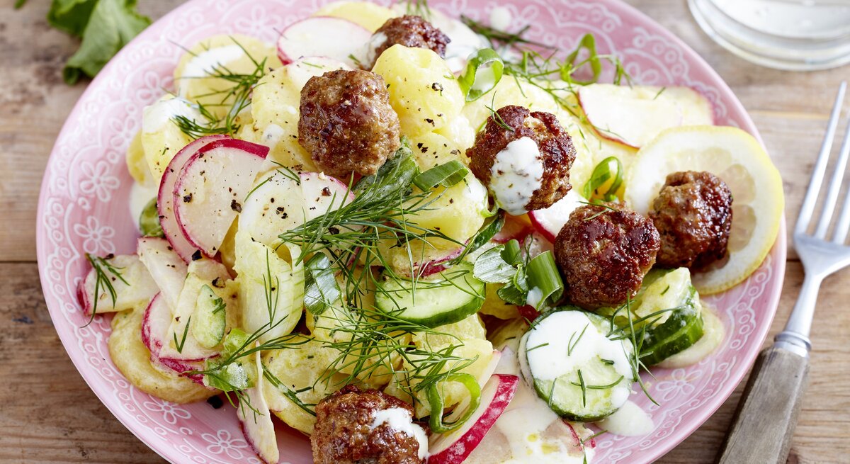 Skandinavischer Kartoffelsalat mit frischem Dill, Skyr, Zitronensaft, Radieschen, Gurke und Lauchzwiebeln, garniert mit kross angebratenen kleinen Frikadellen. 