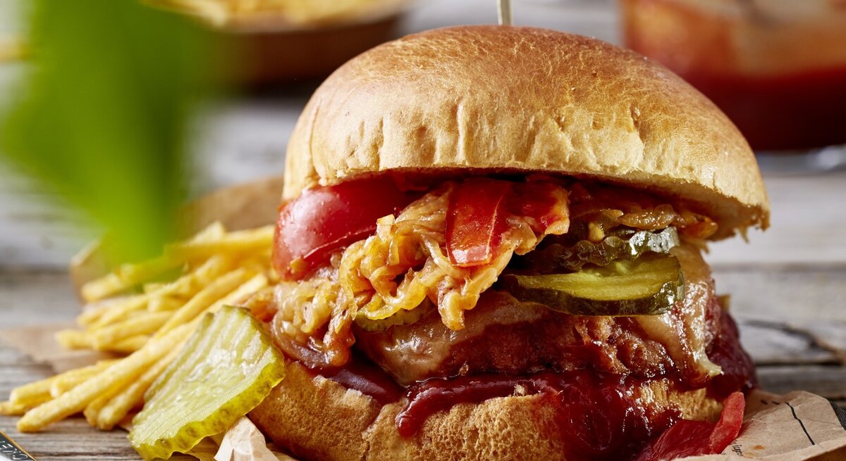 Camping-Burger auf Papier mit Kartoffel-Sticks im Hintergrund auf Holzuntergrund. 