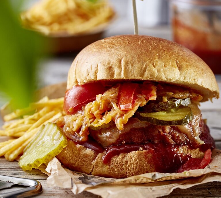 Camping-Burger auf Papier mit Kartoffel-Sticks im Hintergrund auf Holzuntergrund.  | © EAT CLUB / Isabell Triemer