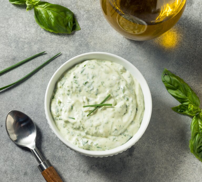 Eine Schale mit Kräuter-Mayonnaise. Daneben steht eine Karaffe Öl und einige Kräuter liegen daneben. | © Getty Images/bhofack2