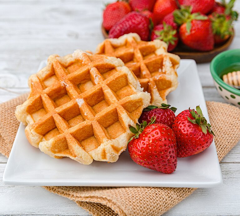 Frontal: Weißer Untergund aus Holt. Darauf liegt ein grobes leinentcuh mit einem weizen Teller. Auf dem sind zwei Haferkleie-Waffeln mit frischen Erdbeeren. Im Hintergrund sind weitere frische Erdbeeren, sowie ein Schälchen mit Honig. | © Getty Images / Phamai Techaphan