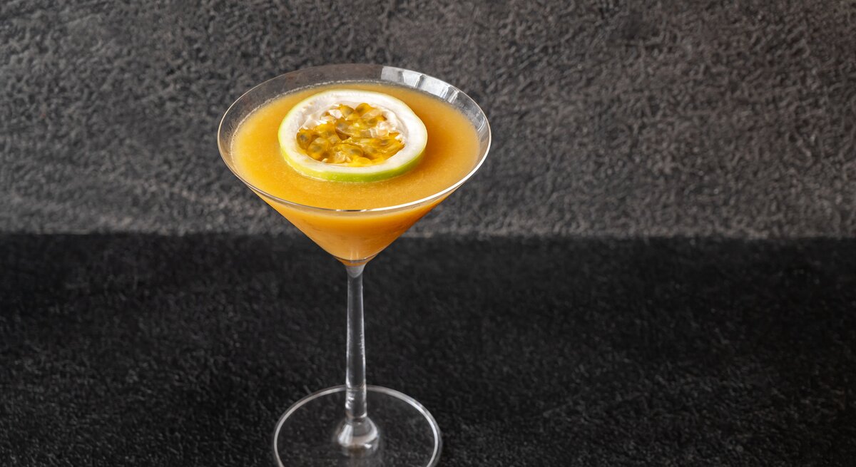Martiniglas gefüllt mit orangefarbenem Cocktail vor dunkler Kulisse.