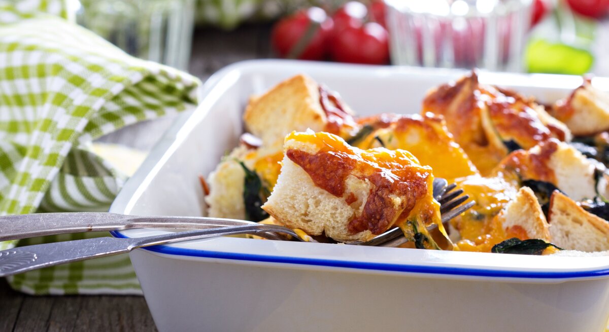 Toast-Mozzarella-Auflauf in weißer Auflaufform, daneben rustikale Dekoration.