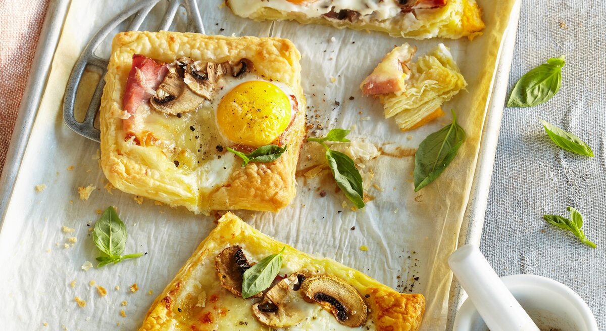 Blätterteigpizzen auf weißem Blech mit Gewürzmörser auf Mikrofaserdecke.