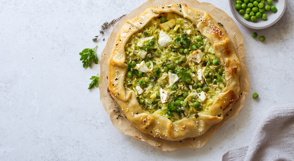 Galette gefüllt mit Kartoffeln, Wirsing und Erbsen, überbacken mit Feta Käse, vor einem hellgrauen Hintergrund von oben.