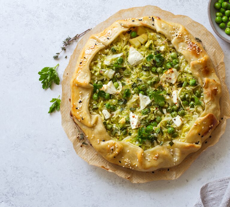 Galette gefüllt mit Kartoffeln, Wirsing und Erbsen, überbacken mit Feta Käse, vor einem hellgrauen Hintergrund von oben. | © GettyImages/annata 78