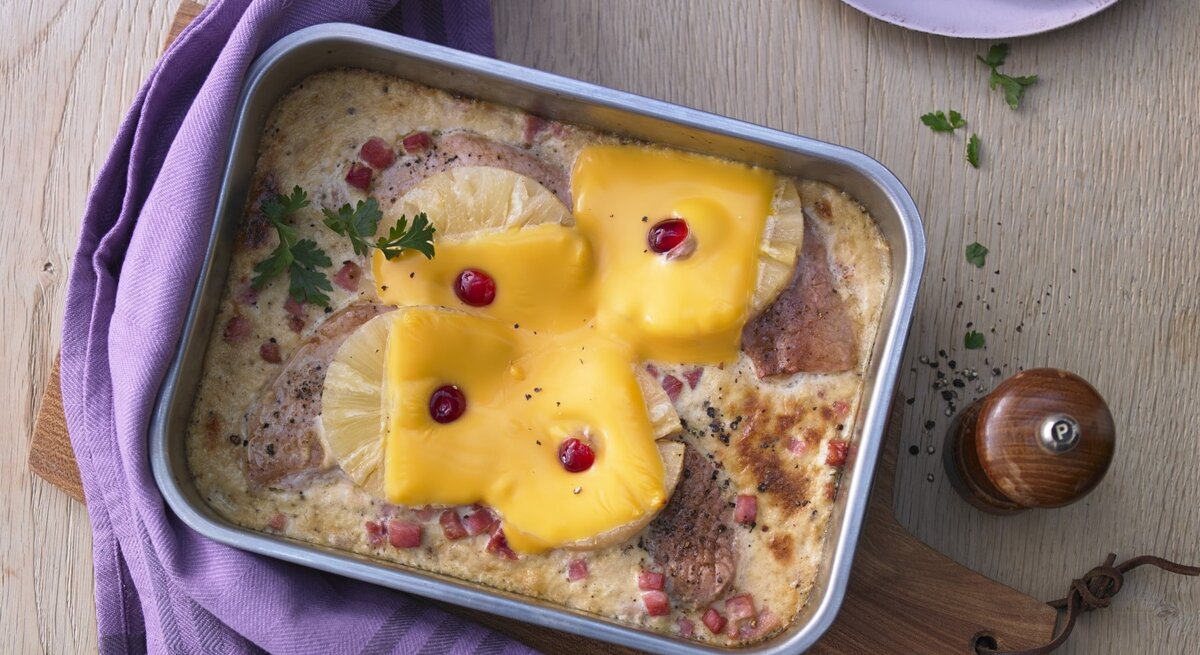 In einer Auflaufform ist ein Hawaii-Schnitzel mit Ananas angerichtet. Es ist mit Petersilie garniert.