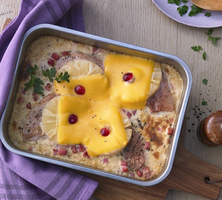 In einer Auflaufform ist ein Hawaii-Schnitzel mit Ananas angerichtet. Es ist mit Petersilie garniert. | © StockFood / Westermann & Buroh Studios