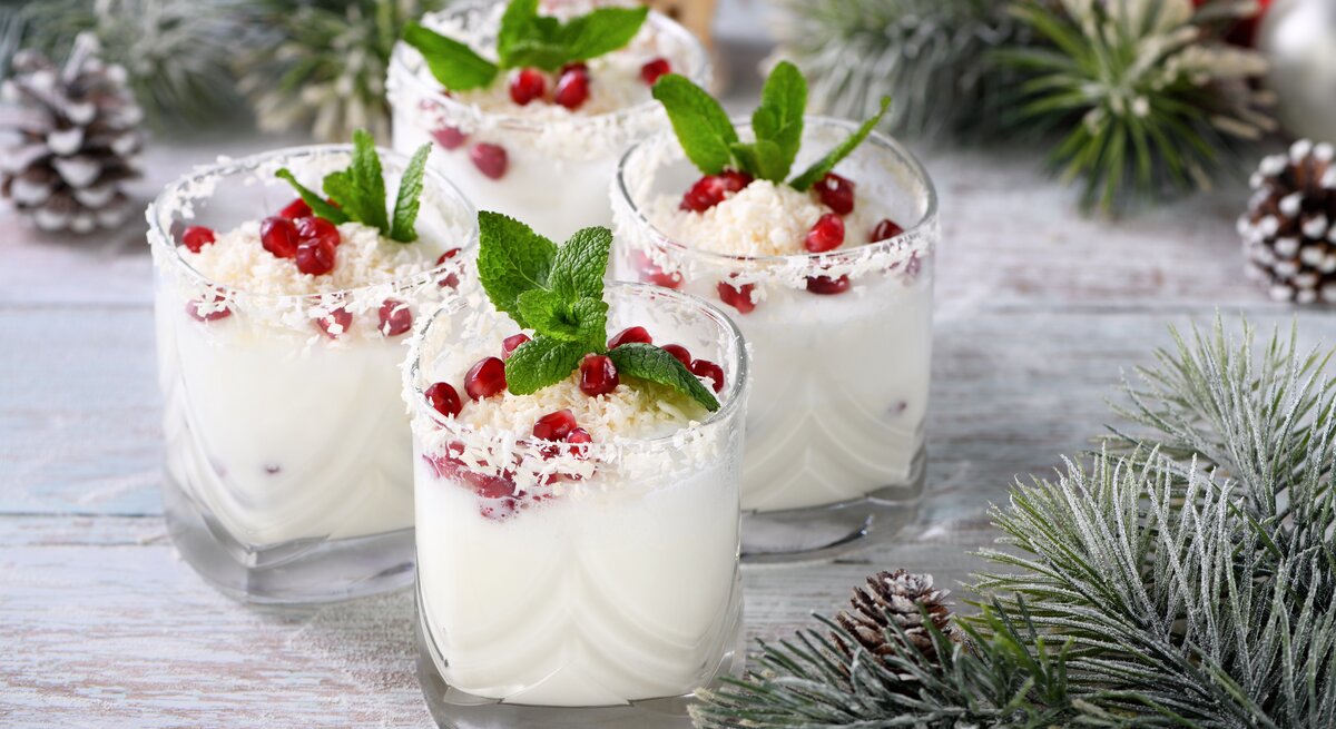 Vier Gläser White Christmas Mojito mit Minze und Granatapfelkernen sowie weißer Schokolade dekoriert. Drumherum weihnachtliche Deko.
