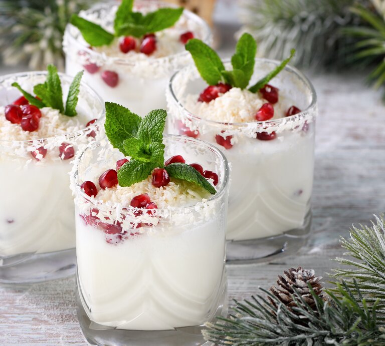 Vier Gläser White Christmas Mojito mit Minze und Granatapfelkernen sowie weißer Schokolade dekoriert. Drumherum weihnachtliche Deko. | © Shutterstock/ apolonia