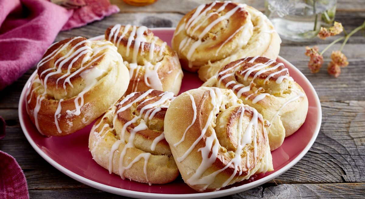 sechs Walnuss-Schmand-Schnecken auf einem teller. Sie sind mit Zuckerguss überzogen. 