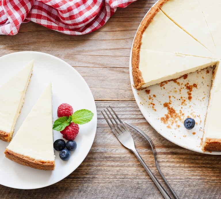 Ein Teller mit zwei Stück veganem New York Cheesecake in der Draufsicht, daneben steht der Kuchen. | © Shutterstock/ Vladislav Noseek