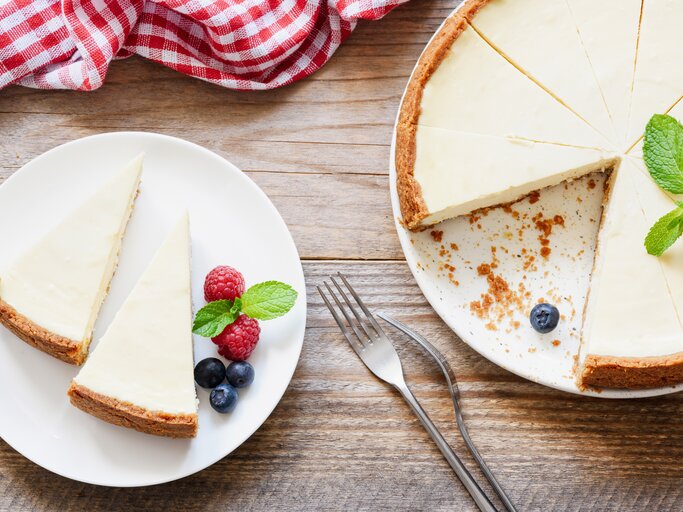 Ein Teller mit zwei Stück veganem New York Cheesecake in der Draufsicht, daneben steht der Kuchen. | © Shutterstock/ Vladislav Noseek