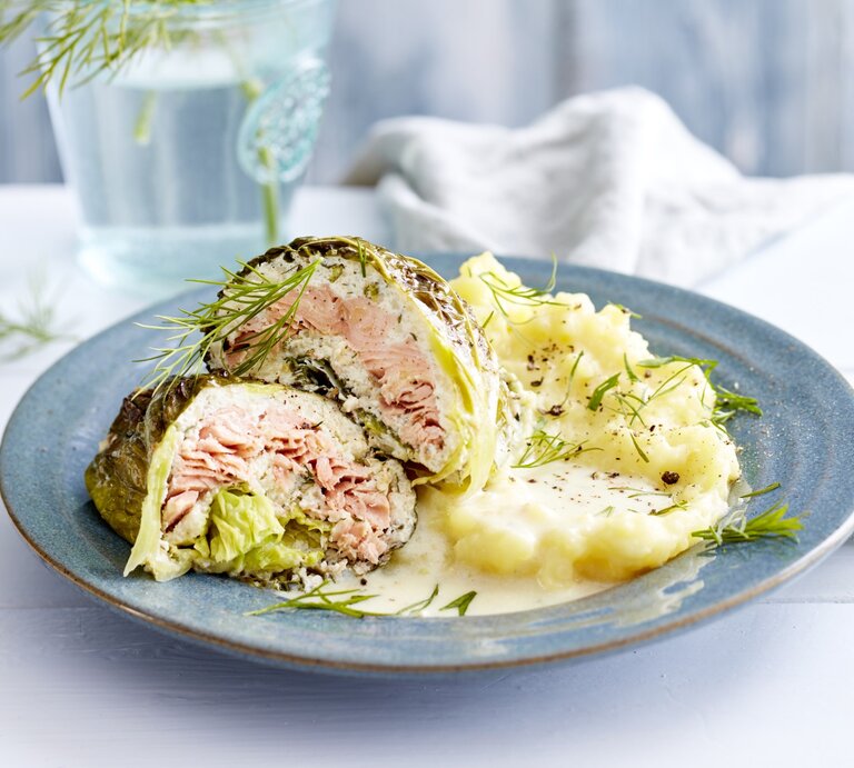 Lachs-Wirsing-Wickel, garniert mit Dill und serviert mit Kartoffelpürree auf einem Tonteller auf weiß gedecktem Tisch.  | © EAT CLUB / Isabell Triemer