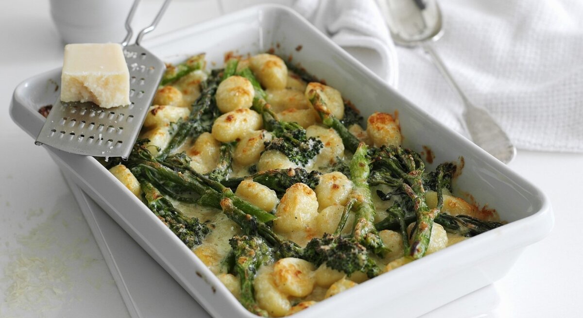 In einer Auflaufform ist ein Brokkoli-Gnocchi mit dreierlei Käse zubereitet. Er ist mit geriebenem Käse überstreut. 