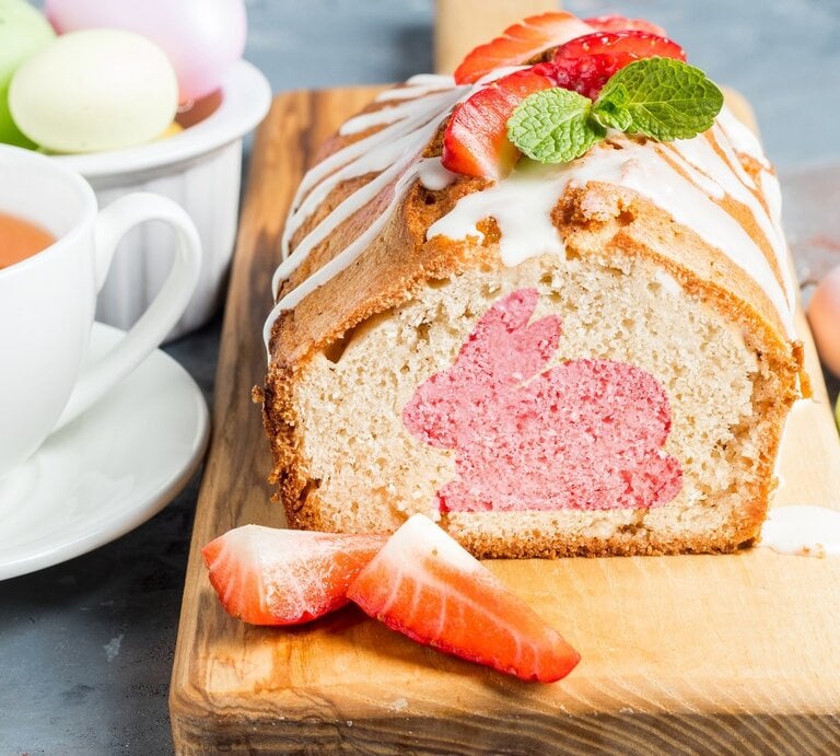 Auf einem Holzbrett liegt ein Osterhasenkuchen aus der Kastenform. Man erkennt einen rosa Hasen im Teig. Der Kuchen ist mit Zuckerguss überzogen.  | © Shutterstock / Anastasia Voskresenskaya