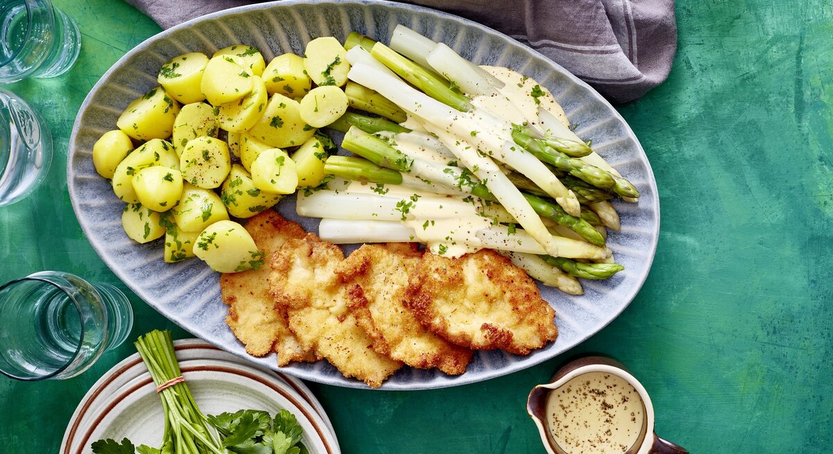 Auf einer Platte ist eine Portion Spargelplatte mit Hähnchenschnitzel angerichtet. Sie ist mit Petersilie verfeinert.