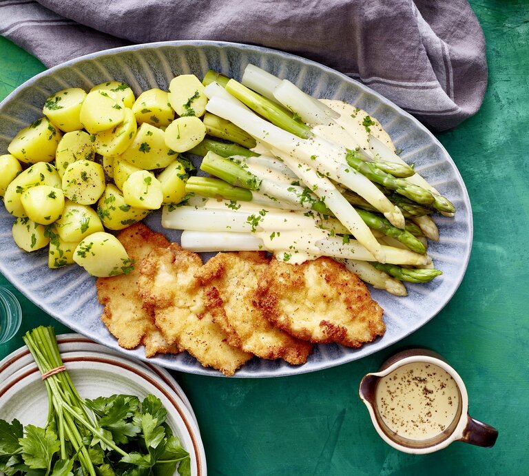 Auf einer Platte ist eine Portion Spargelplatte mit Hähnchenschnitzel angerichtet. Sie ist mit Petersilie verfeinert. | © EAT CLUB / Isabell Triemer