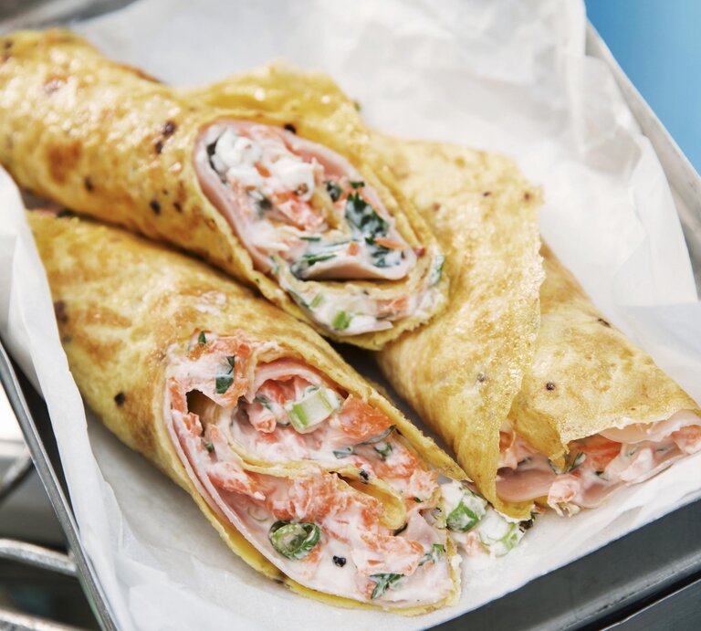 Omelettewraps mit Farmersalat und Schinken aufgeschnitten in einer Blechdose mit Backpapier auf einem Fahrradträger. | © StockFood / ZS Verlag / Theis, Gulliver