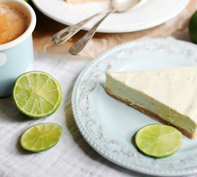 Ein Stück Mojito Torte auf einem Kaffeetisch mit hellblauer Tischdecke und Limetten | © gettyimages/ westend61